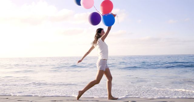 Happy woman holding balloons at the beach in slow motion