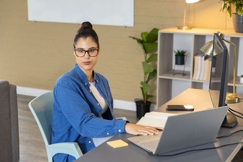 Woman working at laptop in modern home office taking notes, remote work productivity