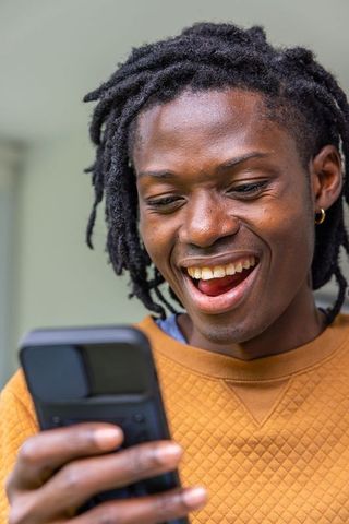 African american man smiling and looking at smartphone wearing mustard quilted sweatshirt