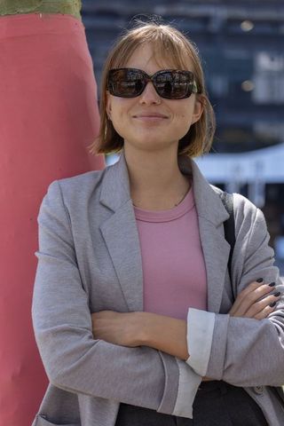 Confident woman standing with arms crossed in urban plaza wearing sunglasses and blazer