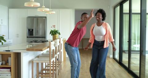 African american couple laughing and dancing together in sunlit modern minimalist kitchen