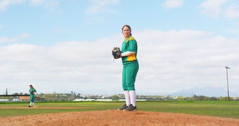 Female softball players in green uniforms on pitcher's mound