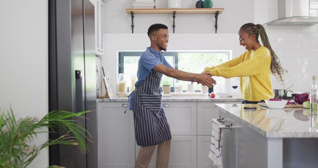 This depicts a cheerful couple enjoying together in the kitchen. The man is wearing a striped apron, while both are dressed in casual clothes. Ideal for promoting family bonding, healthy living, modern kitchens, cooking experiences, or advertisements focusing on happy lifestyles. Perfect for illustrating happiness and fun in everyday domestic moments.