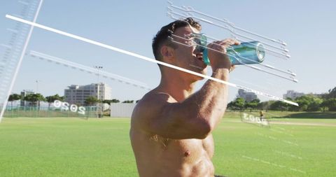 Shirtless athlete drinking from turquoise bottle on sunlit urban sports field