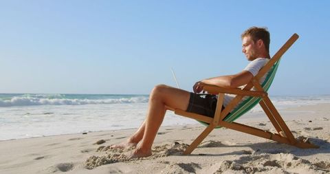 Young Man Using Laptop on Beach in Sunlight