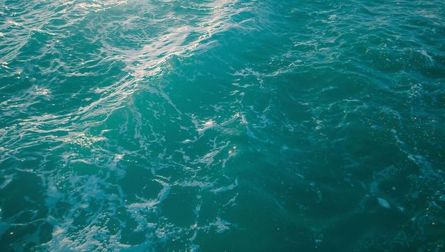 Tranquil greenish-blue sea with gentle ripples and foam patterns