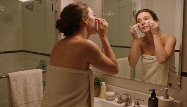 Woman applying under-eye gel patches at bathroom vanity wrapped towel morning skincare ritual