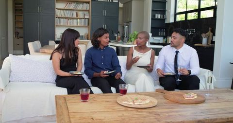 African american friends sharing appetizers on sofa in modern open-plan living room