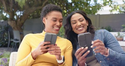 Smiling Women Enjoy Smartphone Together in Sunlit Garden Patio
