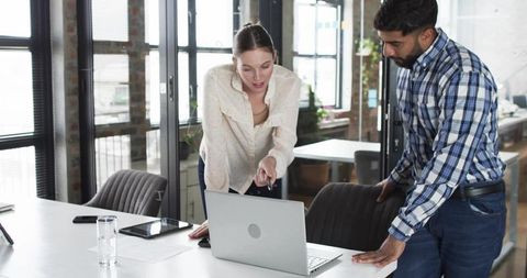 Female colleague pointing at laptop while male coworker reviewing project in modern office