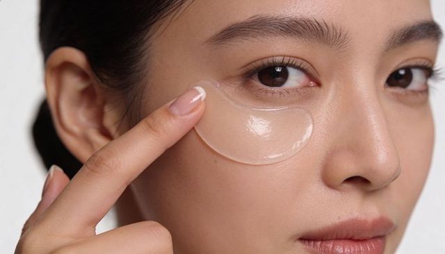 Asian woman applying under-eye hydrogel patch with french manicure for radiant skin closeup