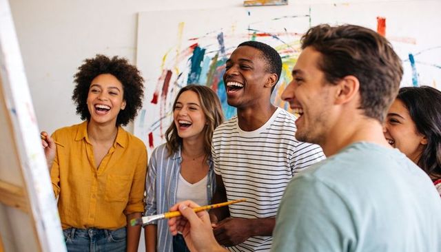 Diverse group laughing and painting together in bright art studio collaborative workshop