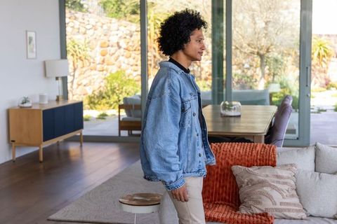 African american man standing by sofa in modern open-plan living room wearing denim jacket
