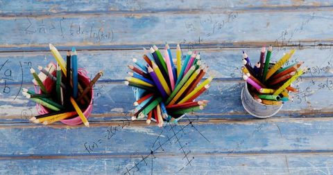 Overhead trio of colorful pencils brimming in cups on rustic blue wood with math sketches