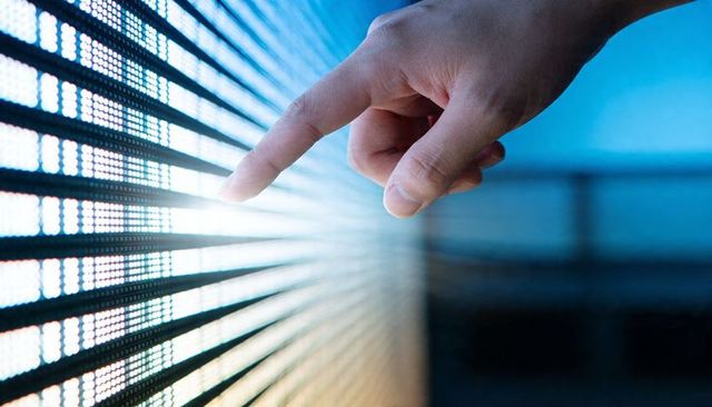 Pressing fingertip across glowing led panel touching interactive digital display