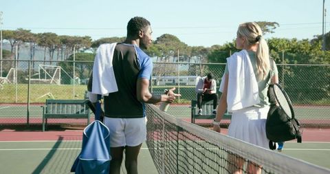 Tennis players walking across net after match carrying rackets duffel bags and towels