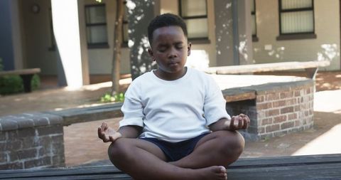 Young african american boy practicing mindful meditation outdoors on bench in courtyard