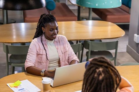 African American women collaborating over laptop in modern cafe coworking space