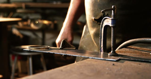 Close-up focusing on a metalworker as they operate a clamp in an industrial workshop. Ideal for content related to manufacturing, tools, trade skills, craftsmanship, industrial professions, and machinery operation.