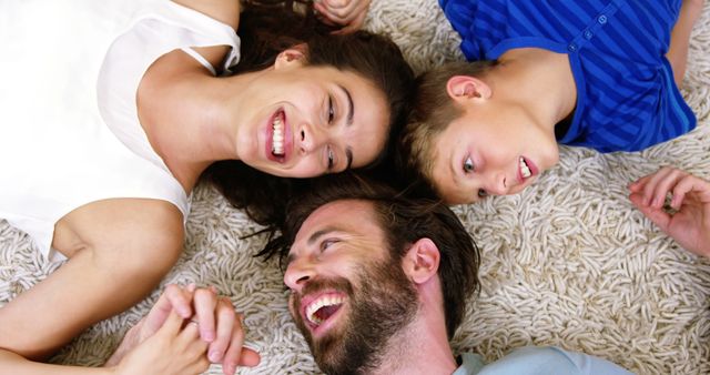 Family laughing and enjoying time together while lying on carpet. Suitable for topics related to family bonding, happiness, and joyful family moments. Can be utilized in family-centered promotions, lifestyle blogs, and home decor advertising.