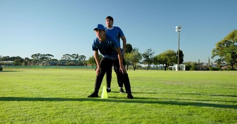Two male athletes practicing outdoor agility drill near cone on grass field