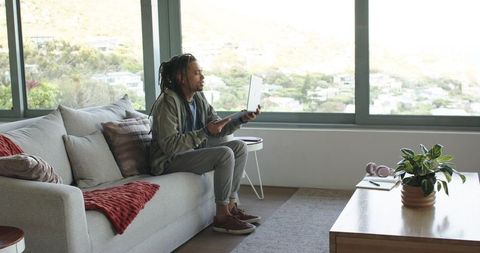 African american man sitting on sofa working remotely with laptop in modern apartment