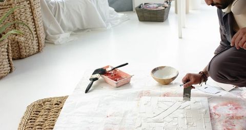 Indian artist smoothing gesso on canvas with metal scraper in bright minimalist studio