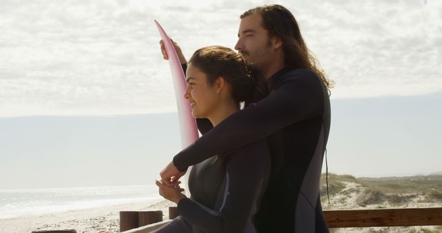 Two surfers wearing wetsuits enjoying the scenic view of the beach. They are standing side by side with surfboards, looking over the ocean horizon. This image can be used for travel blogs, surfing promotional materials, friendship and outdoor activity articles.