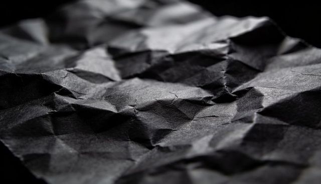 Crumpled black paper texture macro closeup with dramatic highlights and deep shadows