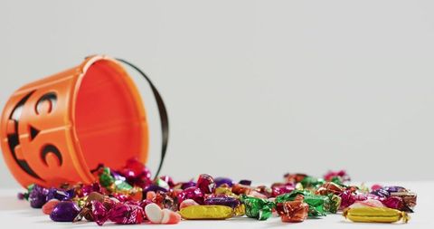Spilling Jack-O'-Lantern Bucket with Colorful Wrapped Candy Across White Tabletop