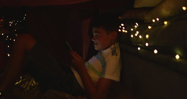 Boy Playing on Digital Device in Blanket Fort with Fairy Lights - Download Free Stock Images Pikwizard.com