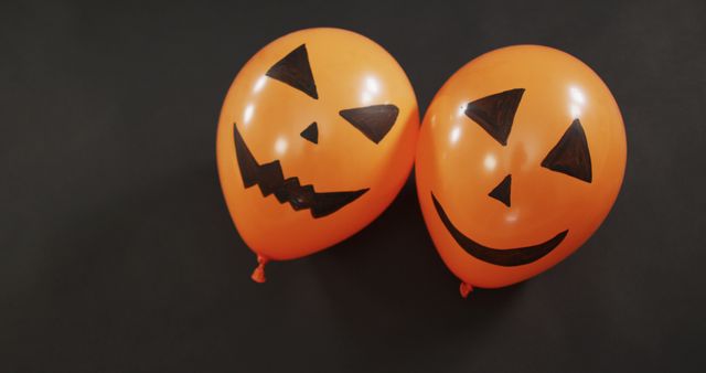 Two orange balloons featuring Jack-o'-lantern faces floating against a black background. Ideal for themes related to Halloween celebrations, decorations, parties, or spooky events for autumn festive vibes.