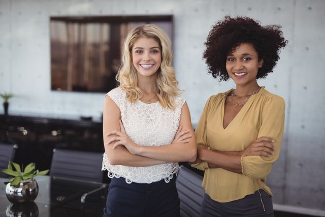 Two professional women standing confidently in a modern office meeting room, smiling at the camera. Ideal for use in business-related content, corporate websites, teamwork and collaboration themes, diversity in the workplace, and professional development materials.