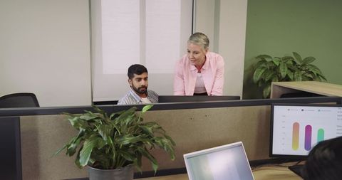 Diverse coworkers collaborating in modern office cubicle with dual monitors