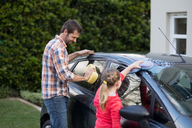 Father and daughter washing car together on a sunny day. Great for illustrating family bonding, teamwork, and outdoor activities. Suitable for use in advertisements, blogs, and articles about family life, car care, and parenting.