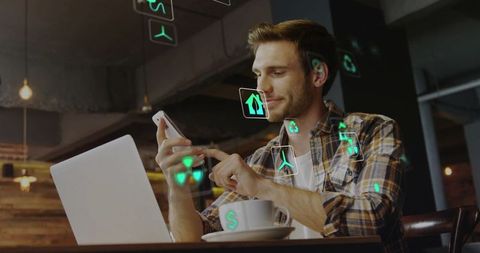 Man tapping smartphone and working on laptop with green ar icons in coffeehouse coworking