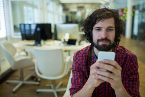Young Professional Engaging With Smartphone in Open Office