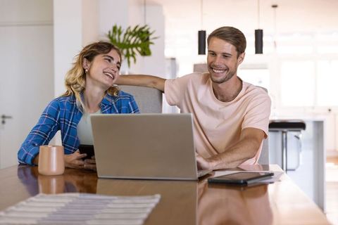 Smiling Couple Collaborating Using Laptop and Smartphone in Modern Kitchen
