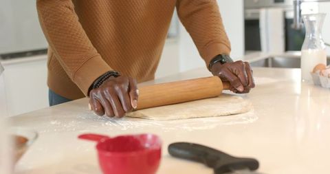 African american man rolling dough with wooden pin on modern kitchen countertop