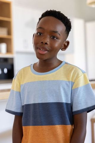 Thoughtful african american boy standing in modern kitchen wearing colorblock striped tee