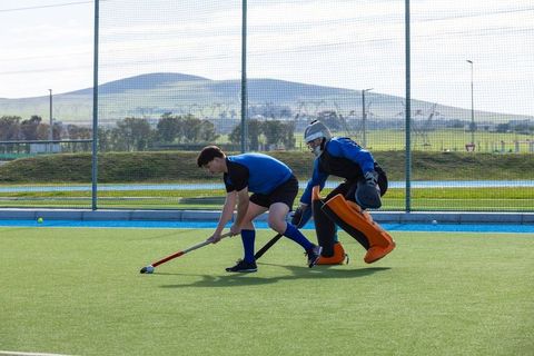 Field hockey action with players and goalkeeper guarding net outdoors