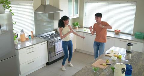 Young couple dancing in bright modern kitchen with island and avocado breakfast prep