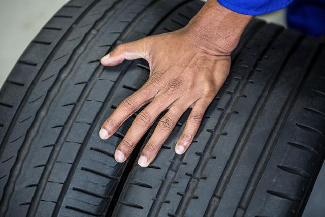 Mechanic's hand touching and inspecting car tyres at a repair garage. Useful for illustrating automotive maintenance, vehicle safety checks, and professional repair services. Ideal for use in articles, advertisements, and websites related to car maintenance, tyre services, and automotive workshops.