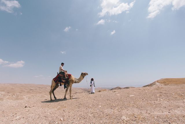 Travelers seen in a vast desert with a camel under the clear, blue sky, perfect for themes related to adventure, travel, exotic locations, or exploring nomadic lifestyles. Useful for travel brochures, adventure blogs, or promoting eco-tourism initiatives.