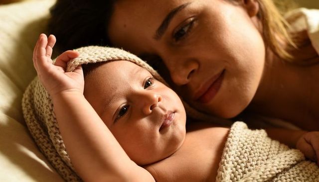 Mother cuddling newborn wearing knit hat and blanket, intimate bonding and serene warmth