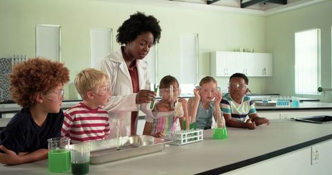 Teacher demonstrating colorful chemistry experiment with children wearing goggles watching