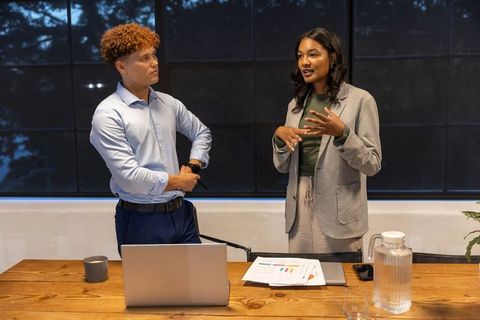 Diverse team presenting data with laptop and charts in modern corporate conference room