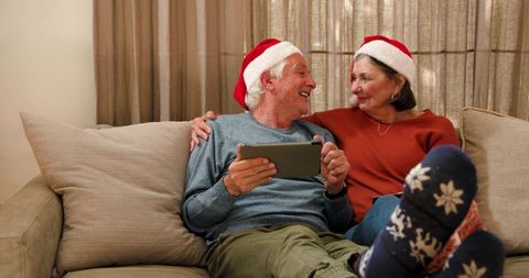 Elderly Couple with Santa Hats Sharing Tablet in Warm Living Room