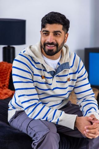 Smiling man in striped hoodie relaxing on sofa with orange throw, minimalist living room
