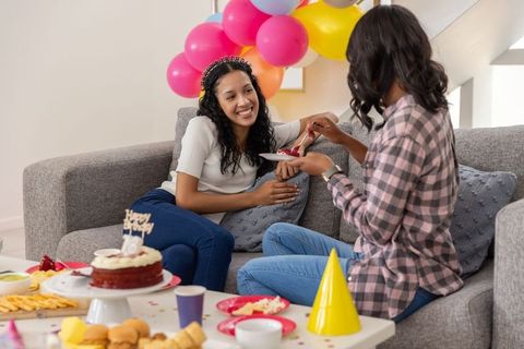 Diverse friends sharing birthday cake on sofa with colorful balloons